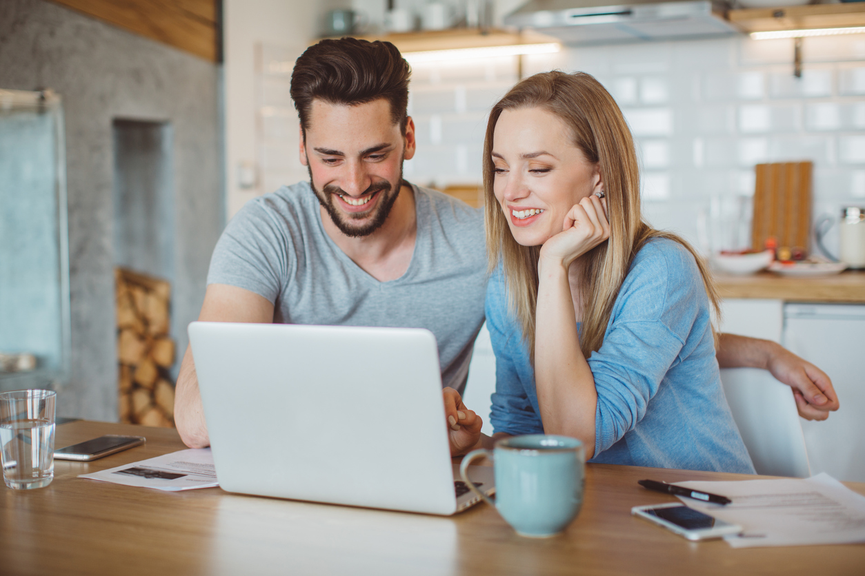 Young couple doing their finances at home. They are wearing pajamas and drinking first coffee of the day at the kitchen.